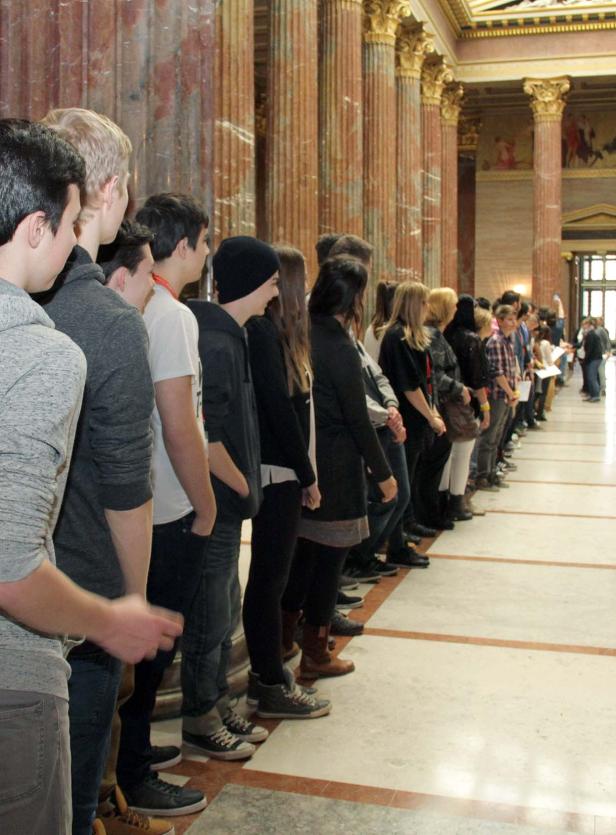 Eine lange Schlange von Menschen steht in einer Halle mit Säulen.