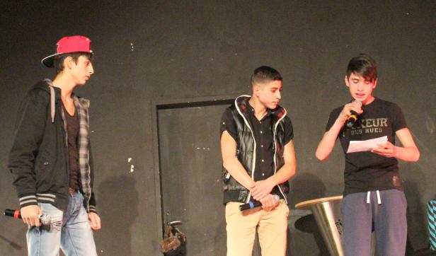 Drei junge Männer stehen auf einer Bühne, einer spricht ins Mikrofon.