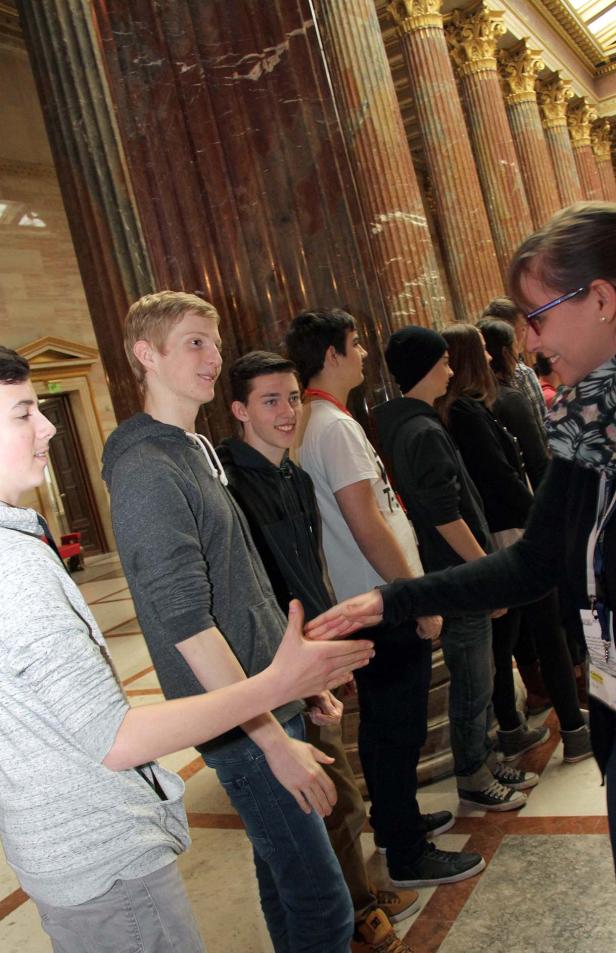 Eine Gruppe junger Leute steht an Säulen und gibt sich die Hände.