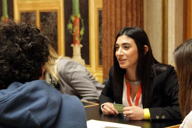 Eine Frau mit dunklen Haaren sitzt an einem Tisch und hält eine grüne Karte in der Hand.