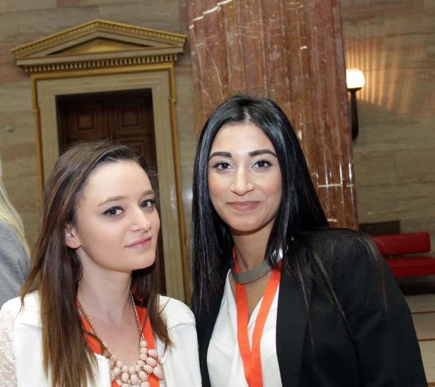 Zwei junge Frauen posieren für ein Foto vor einer verzierten Wand.