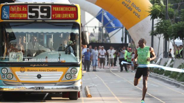 Usain Bolt überquert die Ziellinie bei einem Rennen in Buenos Aires, während ein Bus vorbeifährt.