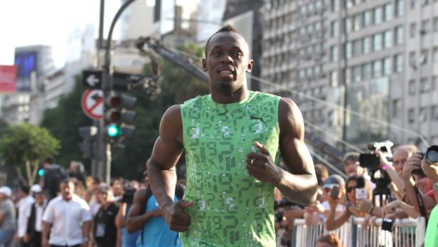 Usain Bolt läuft bei einem öffentlichen Auftritt in einem grünen Trikot.