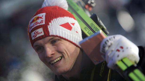 Ein lächelnder Skispringer mit Mütze und Skiern auf der Schulter.