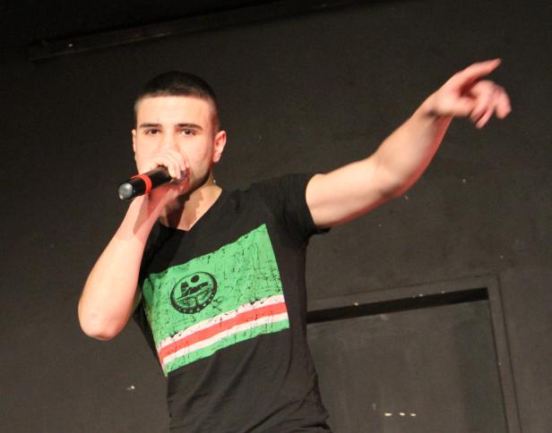 Ein junger Mann singt mit einem Mikrofon in der Hand auf einer Bühne.