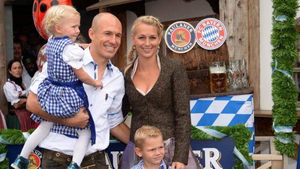 Eine Familie in Tracht vor einem Paulaner- und FC Bayern München-Logo.