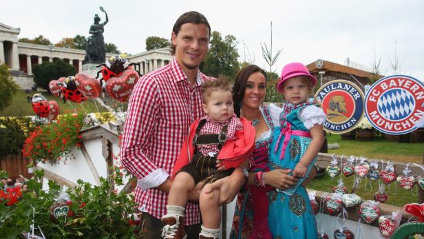 Eine Familie in Tracht posiert vor dem Oktoberfest-Hintergrund mit der Bavaria im Hintergrund.