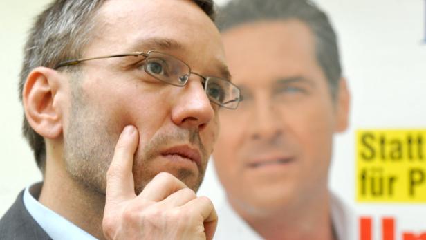 Kickl rückt einmal mehr zur Verteidigung aus. Ein Mann mit Brille denkt nach, im Hintergrund ein Wahlplakat.