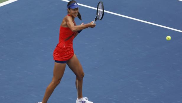 Eine Tennisspielerin in rotem Kleid schlägt einen Ball auf einem blauen Platz.
