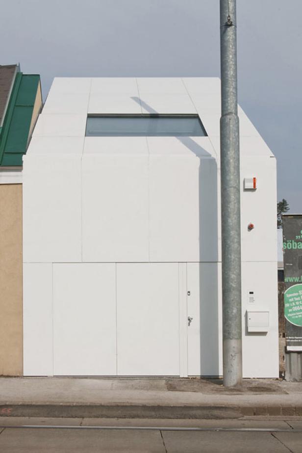 Ein modernes, weißes Gebäude mit einem rechteckigen Fenster und einer schlichten Tür.