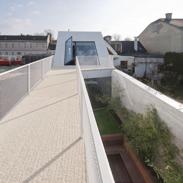 Ein modernes, weißes Haus mit einem erhöhten Gehweg und einem versenkten Garten.