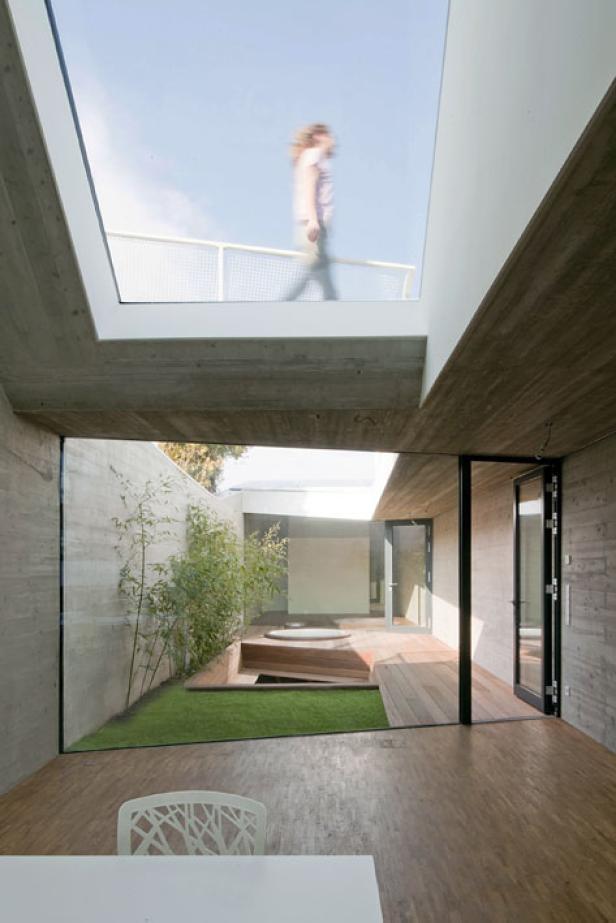 Blick in einen modernen Innenhof mit Holzterrasse und einer Person auf einer Dachterrasse im Hintergrund.