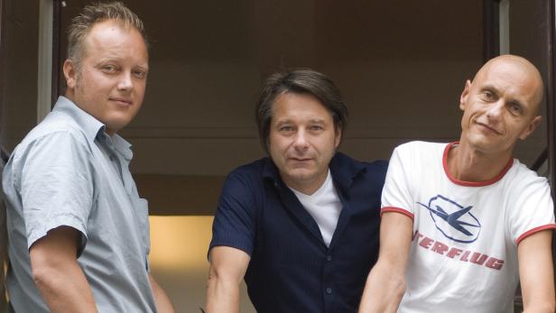 Drei Männer posieren vor einem Fenster.