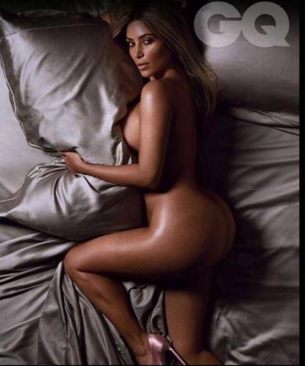 Kim Kardashian liegt auf einem Bett mit grauer Seidenbettwäsche für ein GQ-Fotoshooting.