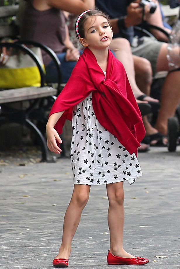 Ein junges Mädchen mit roter Stola und geblümtem Kleid steht im Freien.