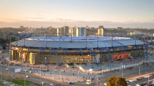 Das Metalist-Stadion. Das Stadion mit blauen Stahlträgern liegt in einer Stadtlandschaft.