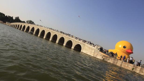 Eine riesige gelbe Gummiente schwimmt neben einer belebten Brücke.