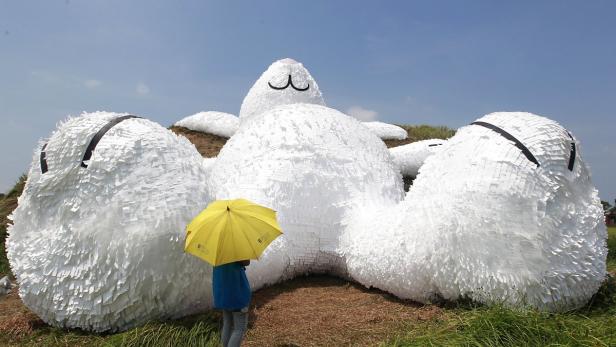 Eine Person mit gelbem Regenschirm steht vor einer riesigen, liegenden Hasen-Skulptur.