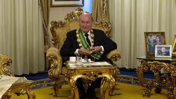 Sepp Blatter sitzt in einem goldenen Sessel mit einer Tasse und einem Glas Wasser auf dem Tisch.
