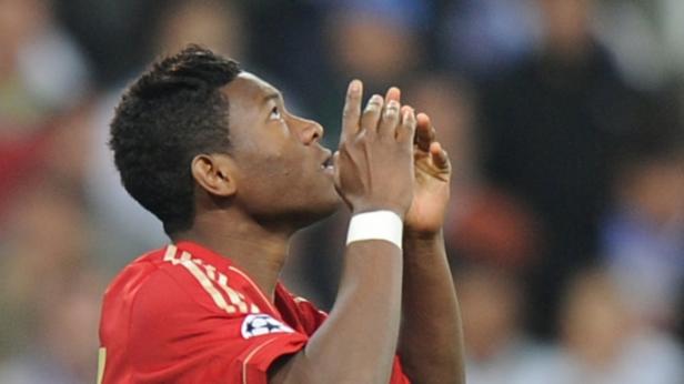 David Alaba, im roten Bayern München Trikot, blickt mit erhobenen Händen nach oben.