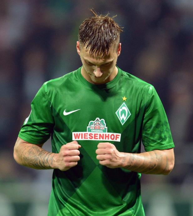 Ein Fußballspieler im grünen Trikot von Werder Bremen mit gesenktem Kopf.