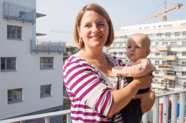 Eine Frau hält ein Baby auf einem Balkon vor einem im Bau befindlichen Gebäude.
