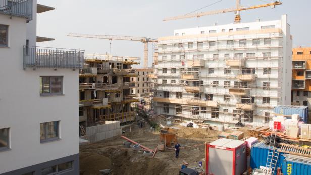 Mehrere Mehrfamilienhäuser befinden sich im Bau, mit Kränen im Hintergrund.