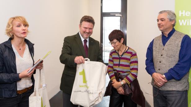 Vier Personen stehen in einem Raum, eine Tasche mit der Aufschrift „Seestadt“ wird überreicht.