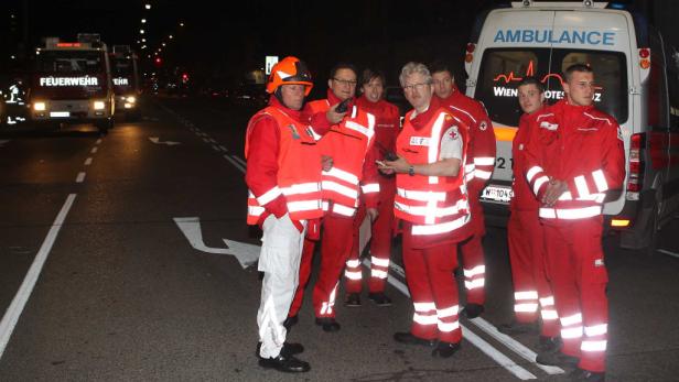 Einsatzkräfte von Feuerwehr und Rettungsdienst stehen nachts auf einer Straße.