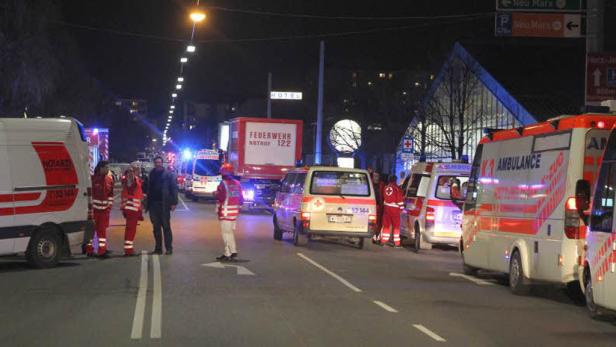 Mehrere Krankenwagen und ein Feuerwehrfahrzeug stehen nachts auf einer belebten Straße.