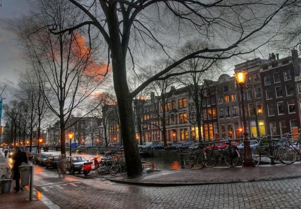 Eine abendliche Szene in Amsterdam mit einem Kanal, Fahrrädern und beleuchteten Häusern.