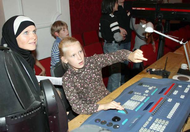 Ein Mädchen bedient ein großes Mischpult, während eine Frau mit Kopftuch zusieht.
