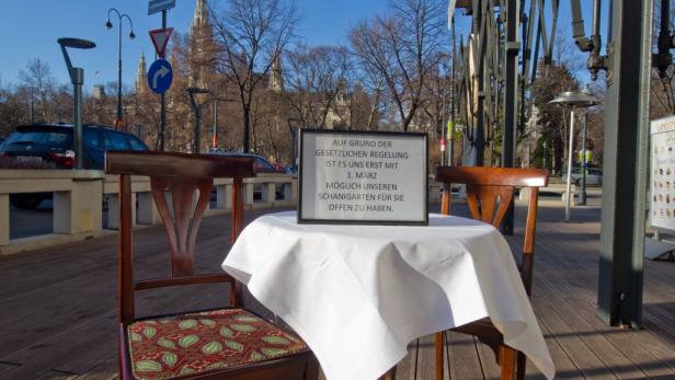 Ein Tisch mit einem Schild, das die verspätete Öffnung eines Schanigartens ankündigt.