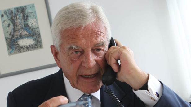 Ein älterer Mann im Anzug telefoniert mit einem schwarzen Telefonhörer.