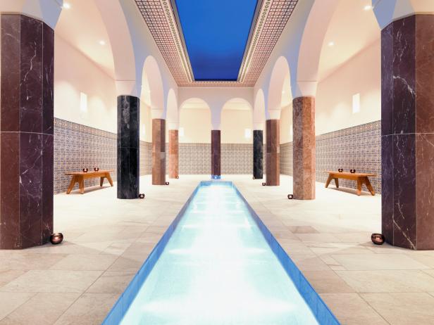 Ein Innenraum mit einem langen, schmalen Pool, umgeben von Säulen und Bänken.