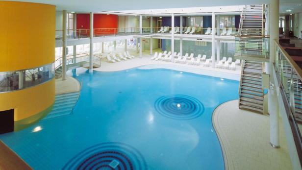 Ein großes Hallenbad mit Liegestühlen auf zwei Ebenen.