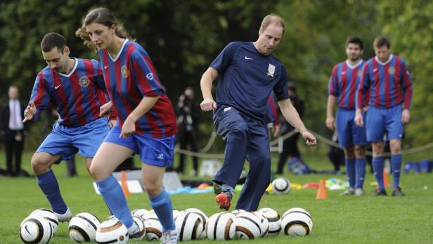 Prinz William absolviert mit anderen Personen ein Fußballtraining auf einem Rasenplatz.