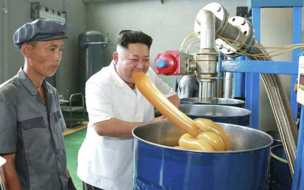 Kim Jong-un scheint eine gelbe Substanz direkt aus einer Produktionsanlage zu probieren, während ein Arbeiter zusieht.