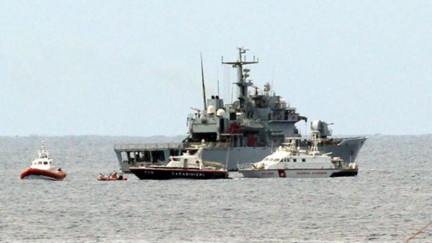 Ein graues Kriegsschiff mit mehreren kleineren Booten auf dem Wasser.