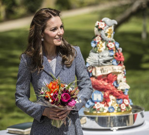 Catherine, Prinzessin von Wales, hält einen Blumenstrauß vor einer verzierten Torte.
