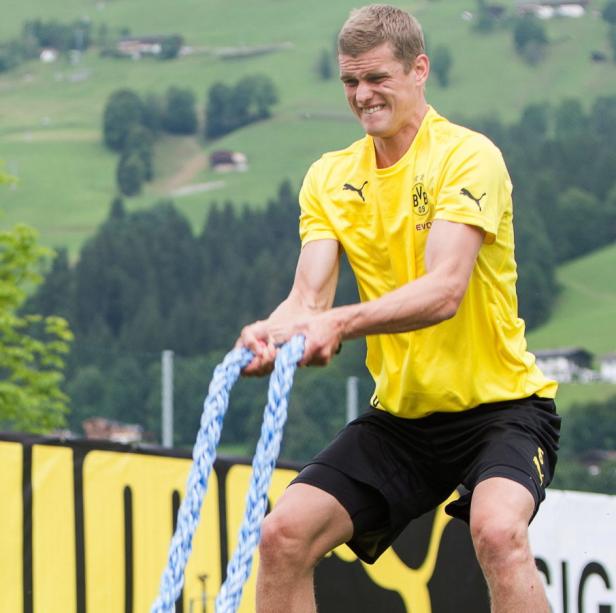 Ein Mann im BVB-Trikot trainiert mit blauen Seilen vor einer grünen Landschaft.