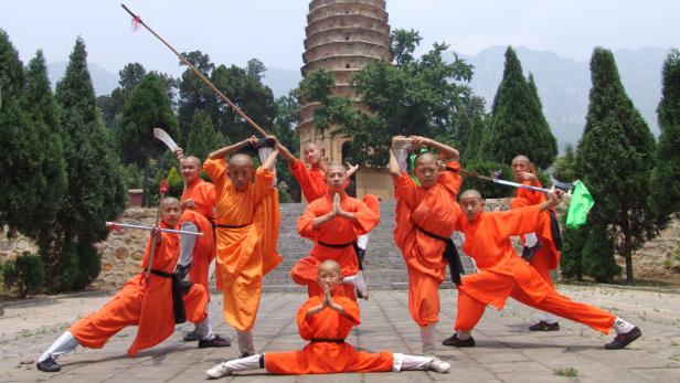 Eine Gruppe Shaolin-Mönche posiert mit Waffen vor einer Pagode.