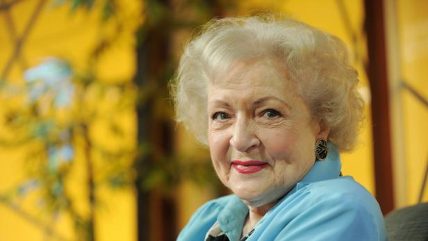 Ein Porträt von Betty White mit einem hellblauen Oberteil vor einem gelben Hintergrund.