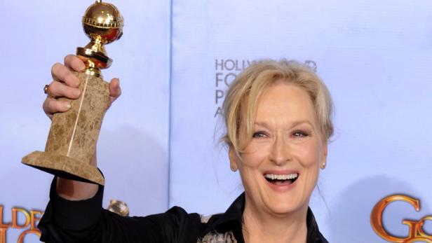 Meryl Streep hält einen Golden Globe Award in die Höhe und lächelt.