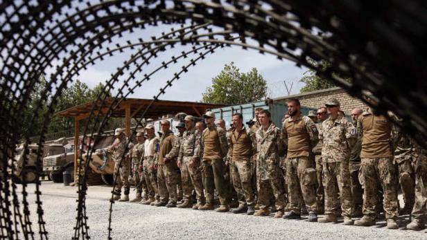 Eine Gruppe Soldaten steht hinter Stacheldraht auf einem Militärgelände.
