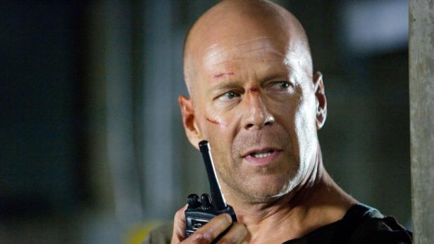 Ein verletzter Bruce Willis hält ein Funkgerät in der Hand.