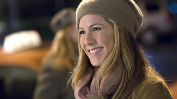 Jennifer Aniston lächelt in einem beigen Hut und Schal.