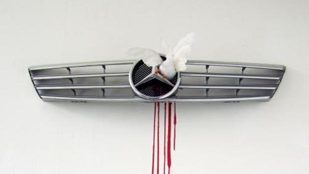 Eine weiße Taube steckt im Kühlergrill eines Mercedes, von dem rote Farbe herunterläuft.
