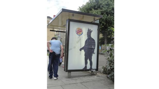 Ein Mann steht an einer Bushaltestelle mit einer Burger King Werbung.