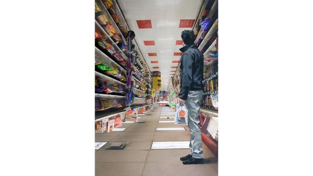 Ein Mann steht in einem Supermarktgang mit Regalen voller Lebensmittel.